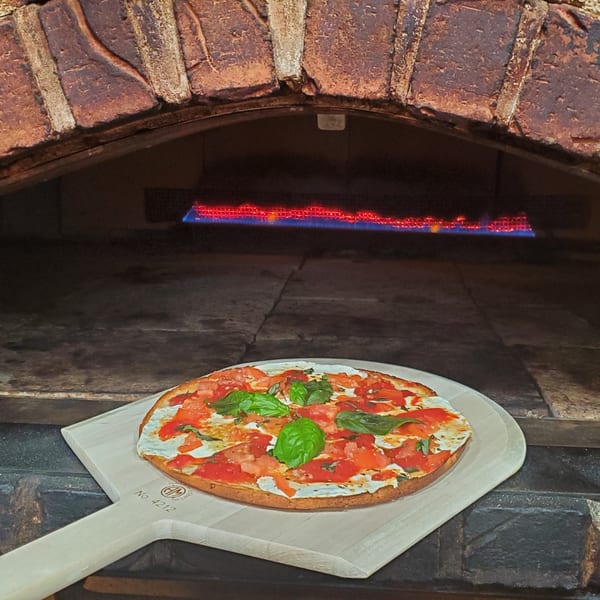Grandpa's Brick Oven Pizza's fresh pizza with tomatoes and basil on a peel, ready for the brick oven.