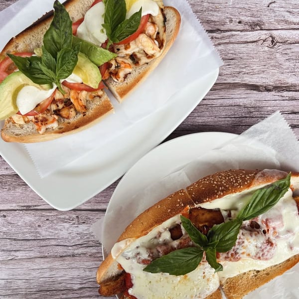Two delicious subs on white plates, one with shrimp and avocado, the other with meatballs and melted cheese.