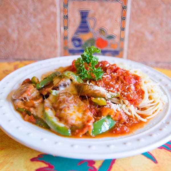 Spaghetti with red sauce, melted cheese, green peppers, and parsley on a white plate.