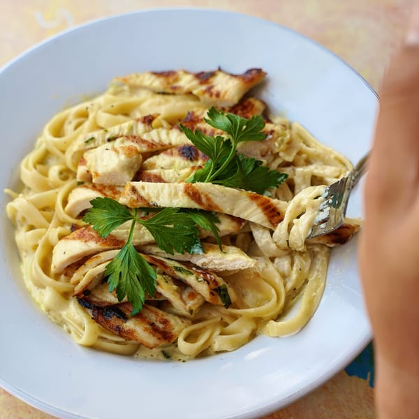 Creamy fettuccine alfredo with grilled chicken strips and fresh parsley on a white plate.
