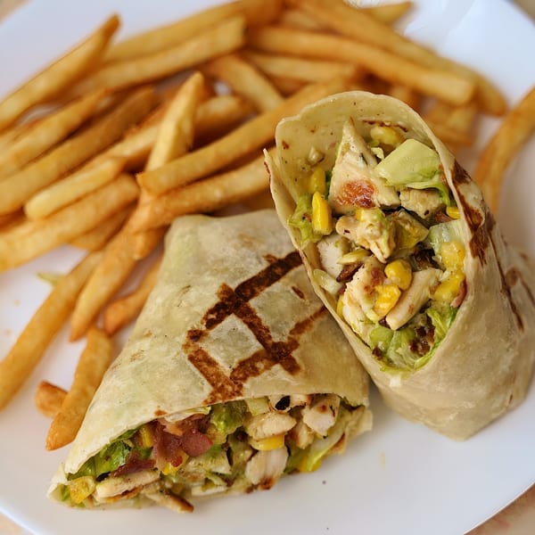 Two grilled chicken wraps filled with corn, avocado, and lettuce, served with french fries.