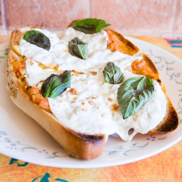 Toasted bread topped with melted cheese, tomato sauce, and fresh basil leaves on a white plate.